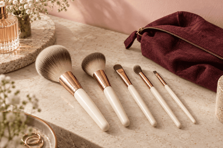 Cinq pinceaux de maquillage et une trousse bordeaux sur une coiffeuse